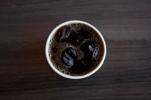 Aerial shot of a refreshing iced coffee in a cup on a wooden surface.