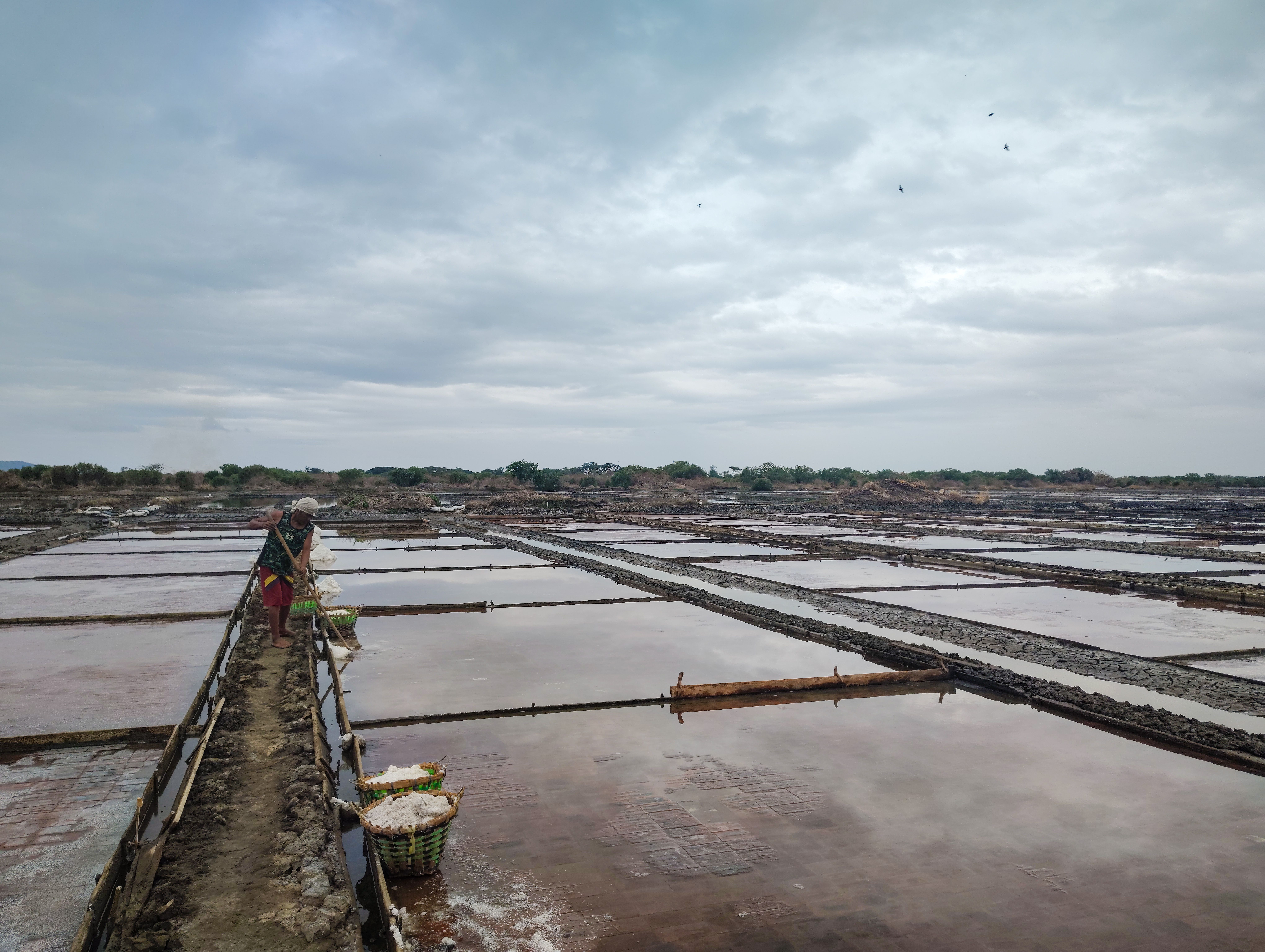 A person working on a traditional salt farm under a cloudy sky in the Philippines.