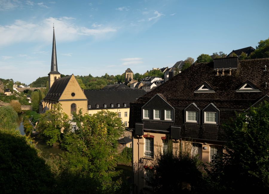 A picturesque view of Luxembourg City featuring historic architecture and lush greenery under a clear blue sky.