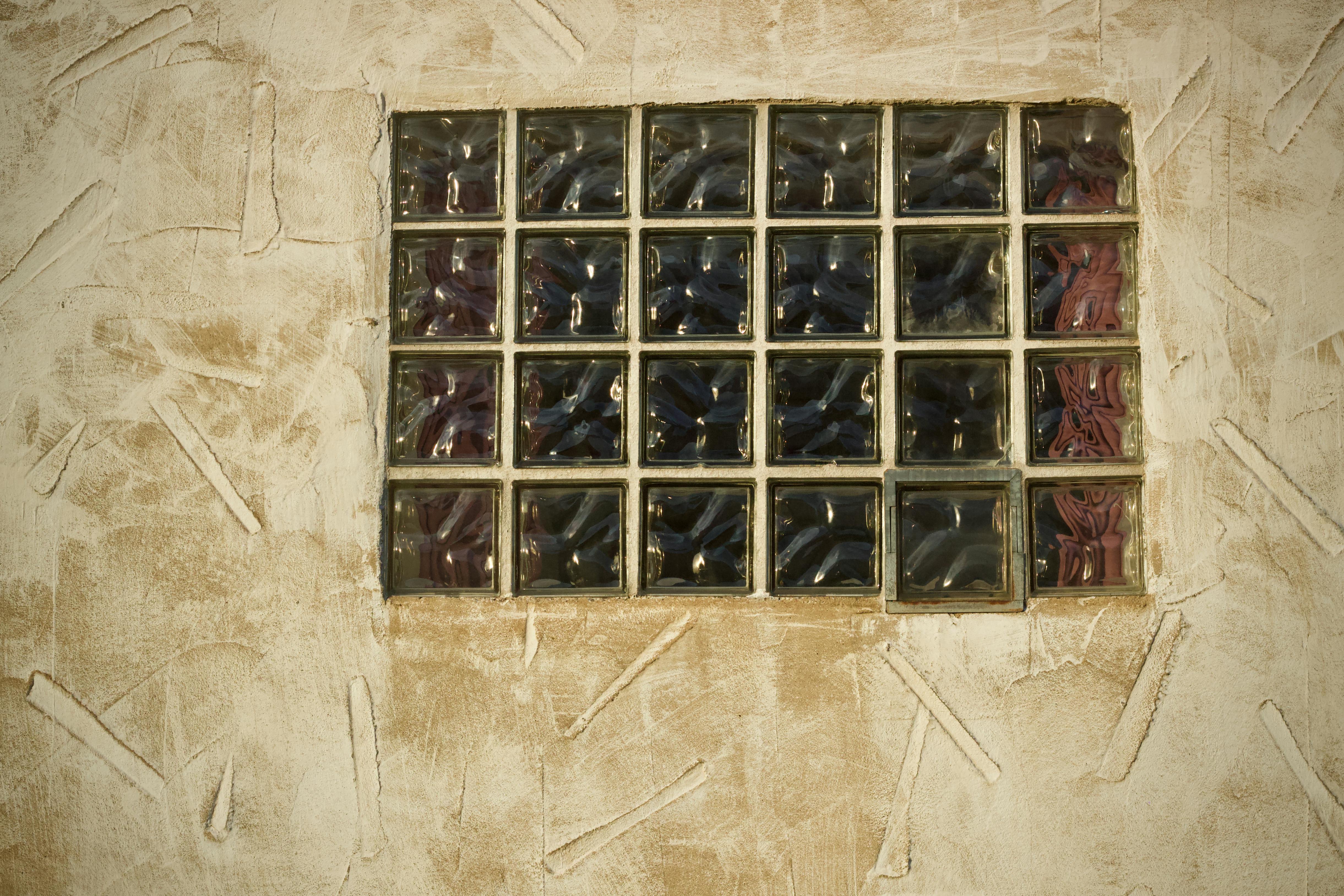 бесплатная Крупный план окна из фактурных стеклянных блоков в бежевой оштукатуренной стене, демонстрирующий художественный дизайн. Стоковое фото