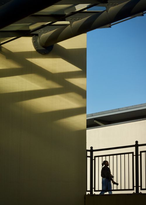 Free Person walking on a bridge against a modern urban structure with strong shadows and clear sky. Stock Photo