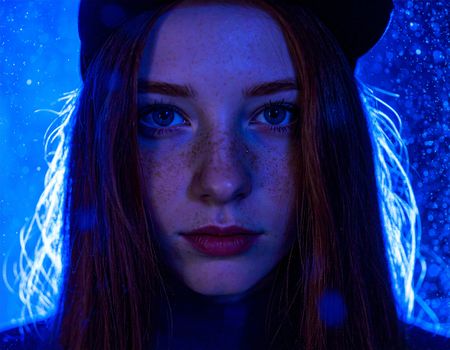 Vibrant artistic portrait of a young woman with freckles, illuminated by blue lighting in Poznań.