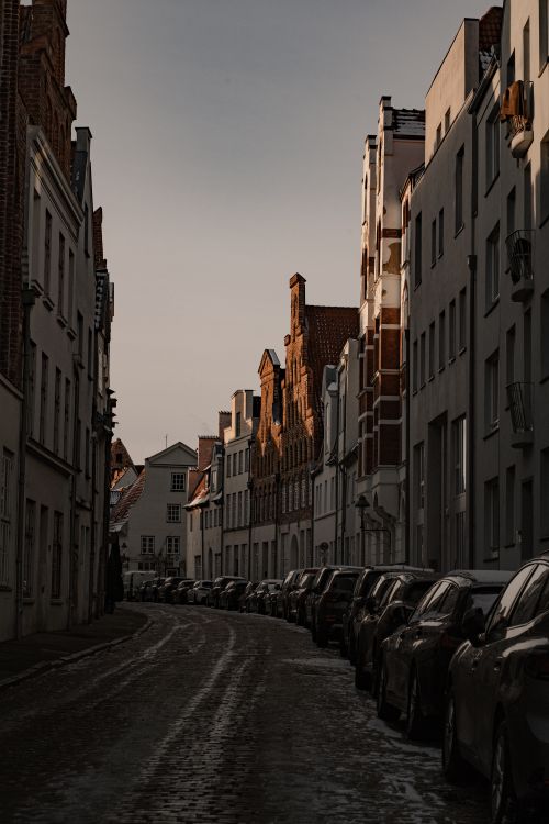 Free Quaint street scene in Lübeck, Germany at sunset, showcasing classic architecture and a row of parked cars. Stock Photo