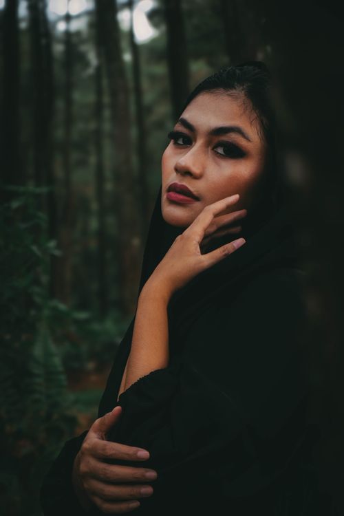 Free A dramatic portrait of a woman with intense gaze wrapped in black, set in a dark forest. Stock Photo