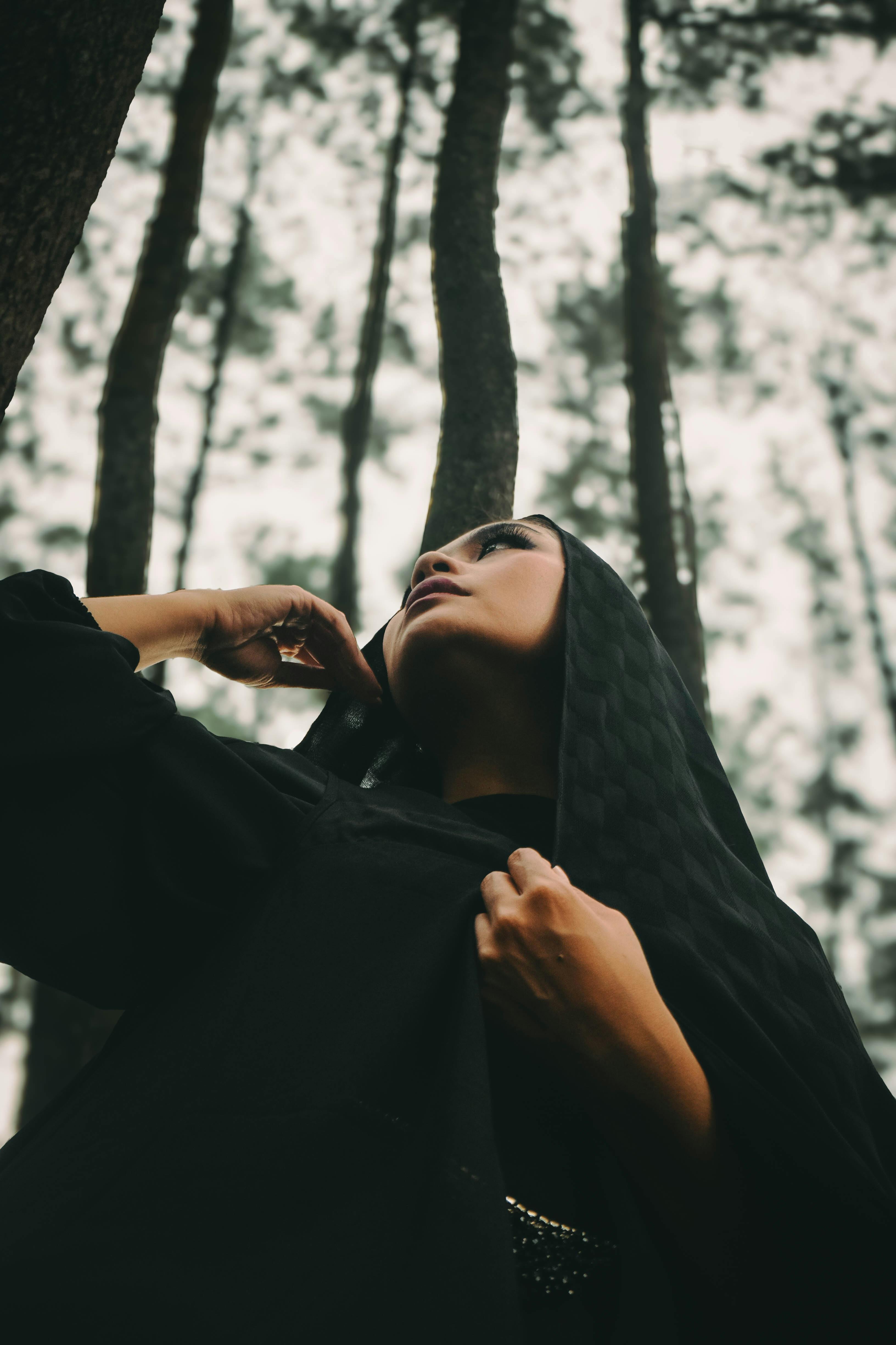 Gratis Retrato dramático de una mujer en un bosque, mirando hacia arriba, envuelta en un velo negro. Foto de stock