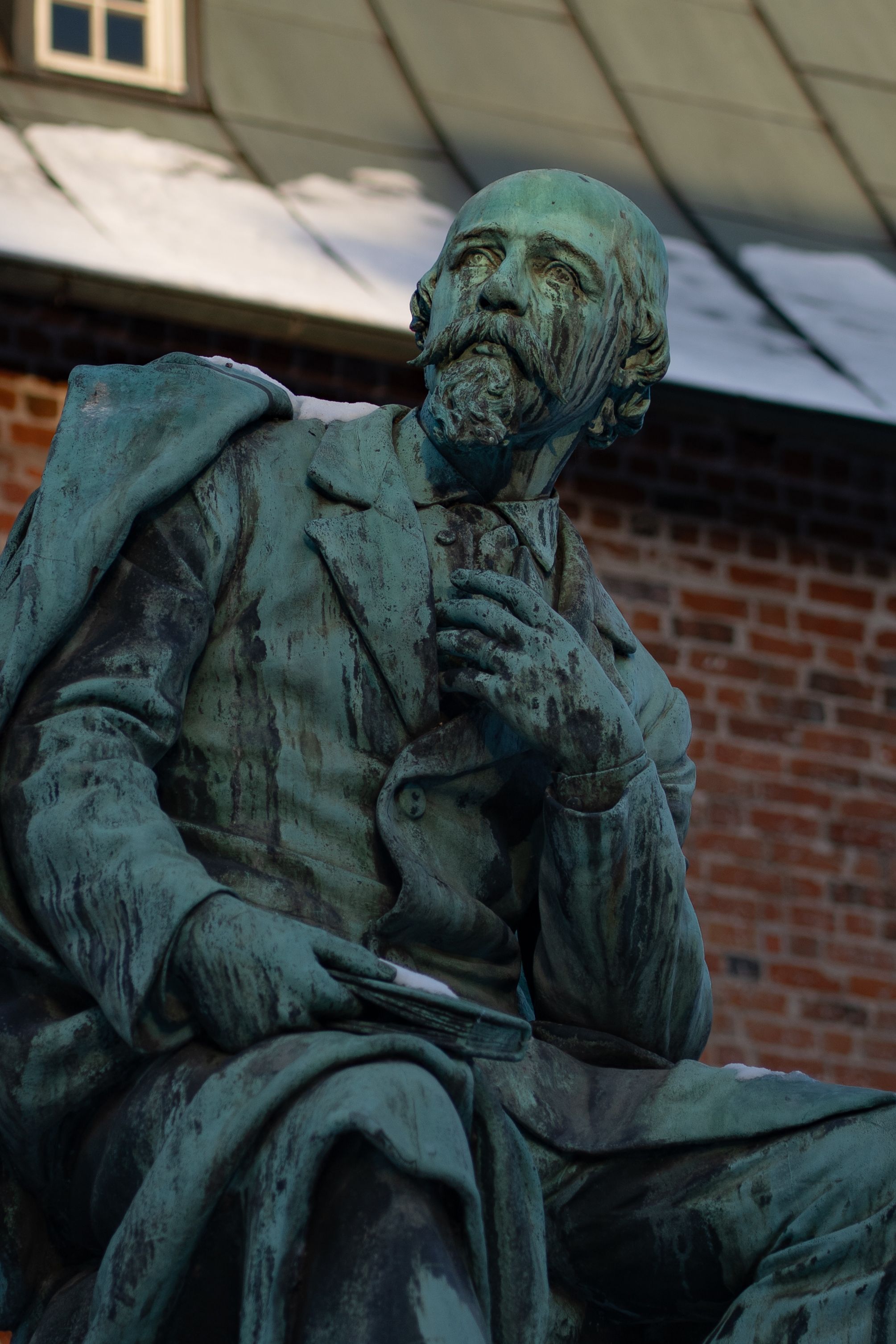 Close-up of a weathered bronze statue of a historical figure against a brick building.
