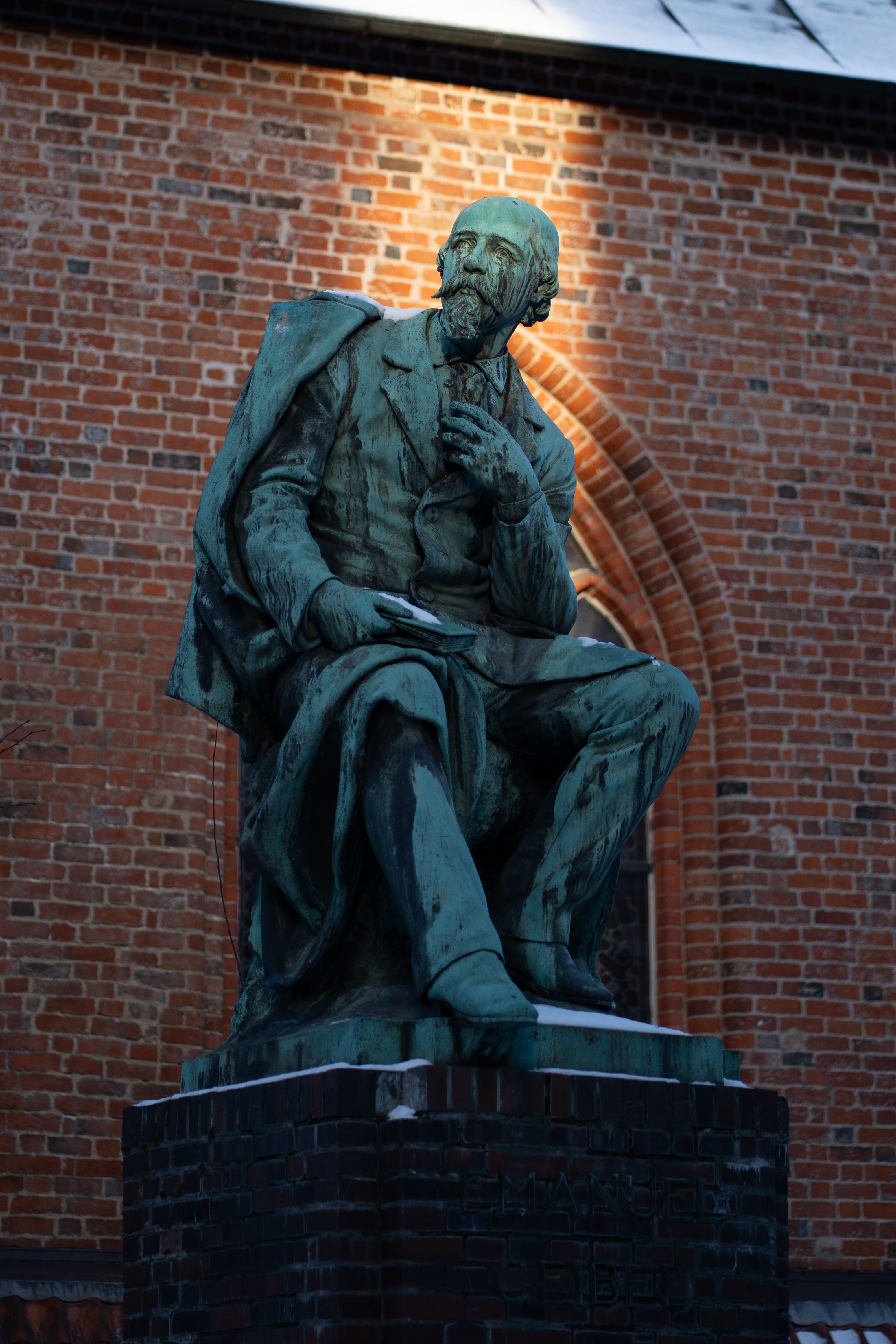 A bronze statue of a seated historical figure in front of a brick wall.