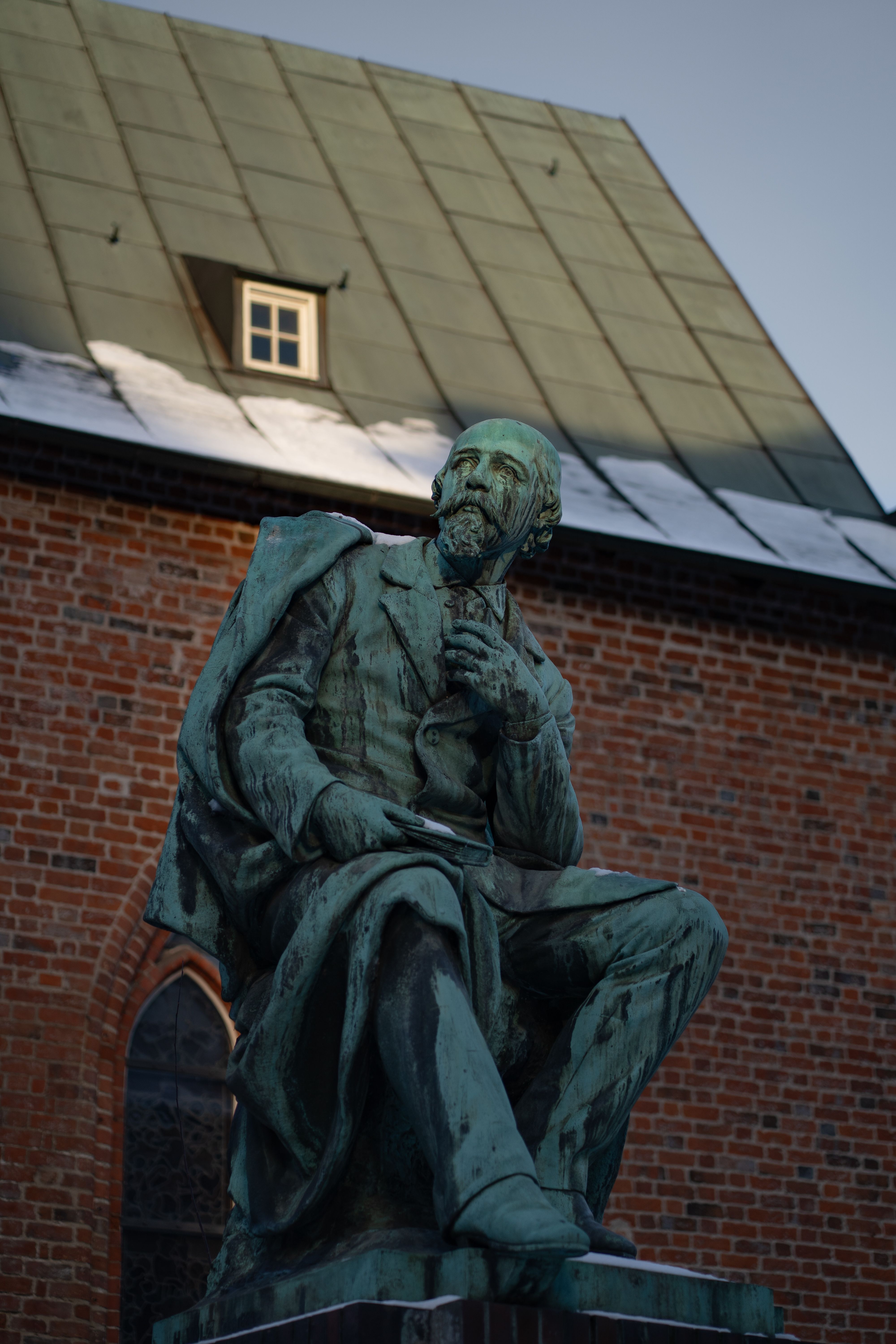 Bronze statue of a contemplative figure on church background with snow.