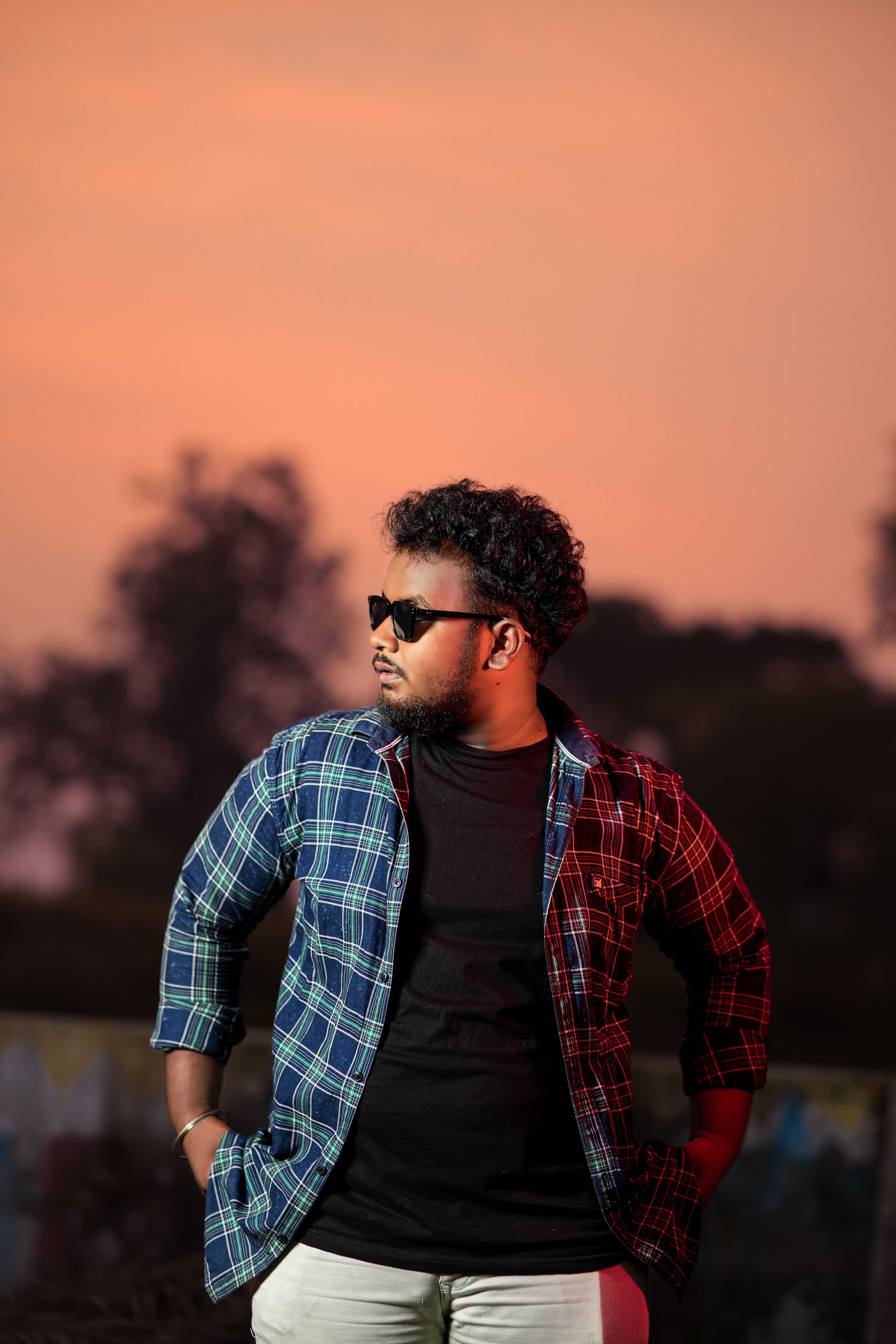 Man posing in sunglasses against a vibrant sunset backdrop outdoors.