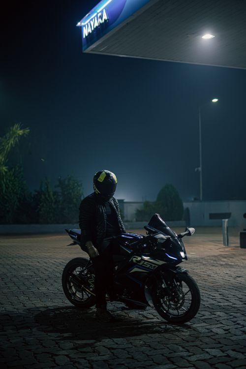 Free Motorcyclist at a gas station at night, under ambient streetlights, showcasing a sleek sports bike. Stock Photo