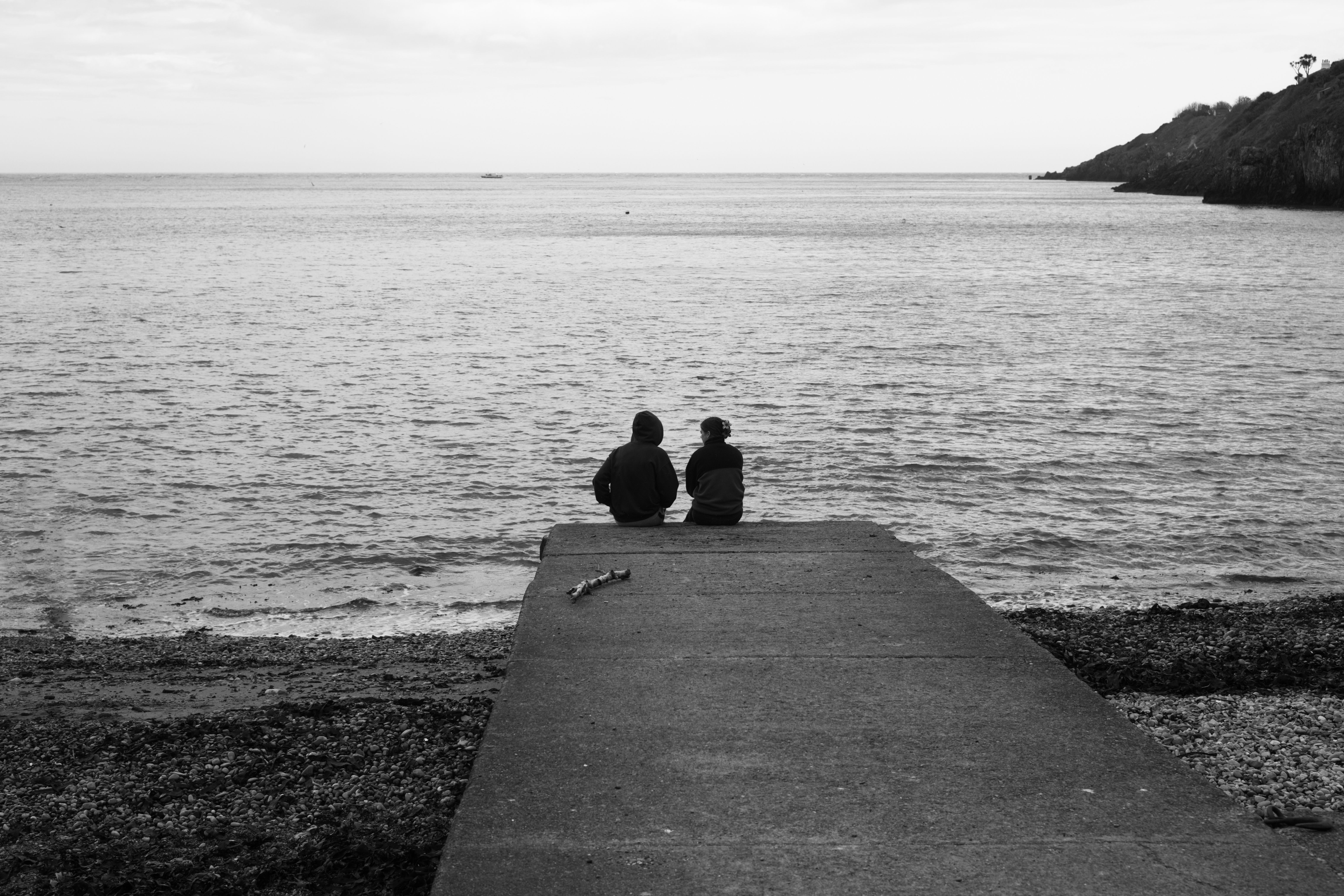 A couple sitting on a pier by the sea in monochrome, radiating peace.