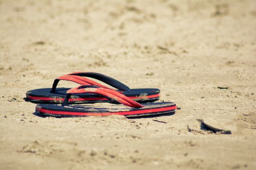 Free Red flip flops resting on a sandy beach capturing the essence of summer relaxation. Stock Photo