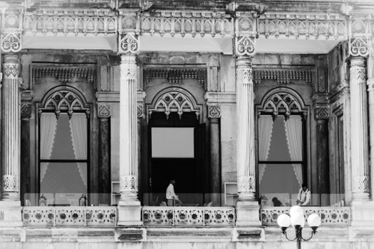 Elegant architectural facade in black and white with people visible on the balcony.