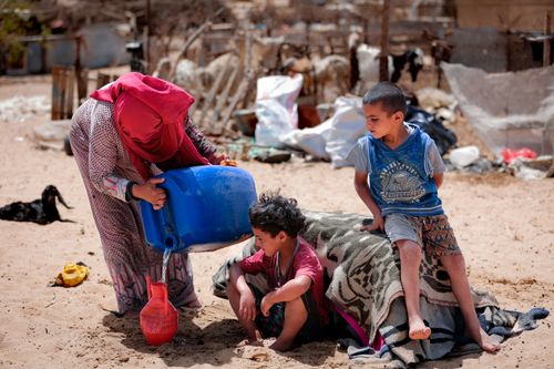 Free A family in Gaza managing everyday tasks under challenging conditions. Water is being poured from a large container. Stock Photo