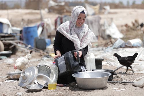 Free A woman in traditional attire washing dishes outdoors in Gaza. Stock Photo