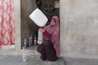 Middle Eastern woman pouring water indoors in Gaza. Depicts daily life and resourcefulness.