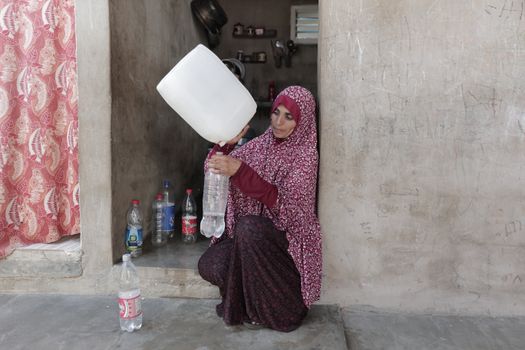 Middle Eastern woman pouring water indoors in Gaza. Depicts daily life and resourcefulness.
