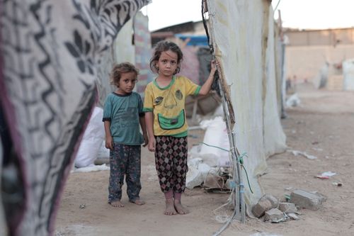 Free Two children stand together amidst a refugee camp setting in Gaza, showcasing resilience and hardship. Stock Photo