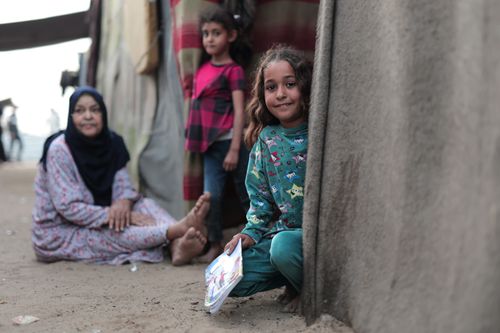 Free Heartwarming scene of children in Gaza smiling near their home with a nurturing adult close by. Stock Photo