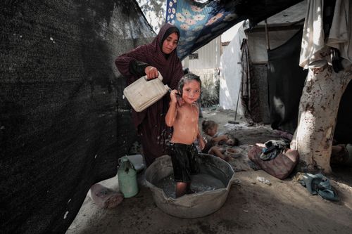 Free A woman bathes her child outdoors in a makeshift setup in Gaza. Stock Photo