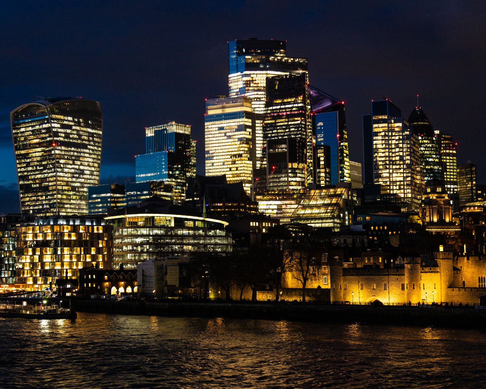 Dazzling night skyline of London featuring modern skyscrapers and city lights reflecting on the Thames.