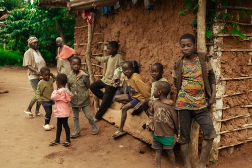 Free A group of children and adults gather outside a traditional mud house in a vibrant village setting. Stock Photo