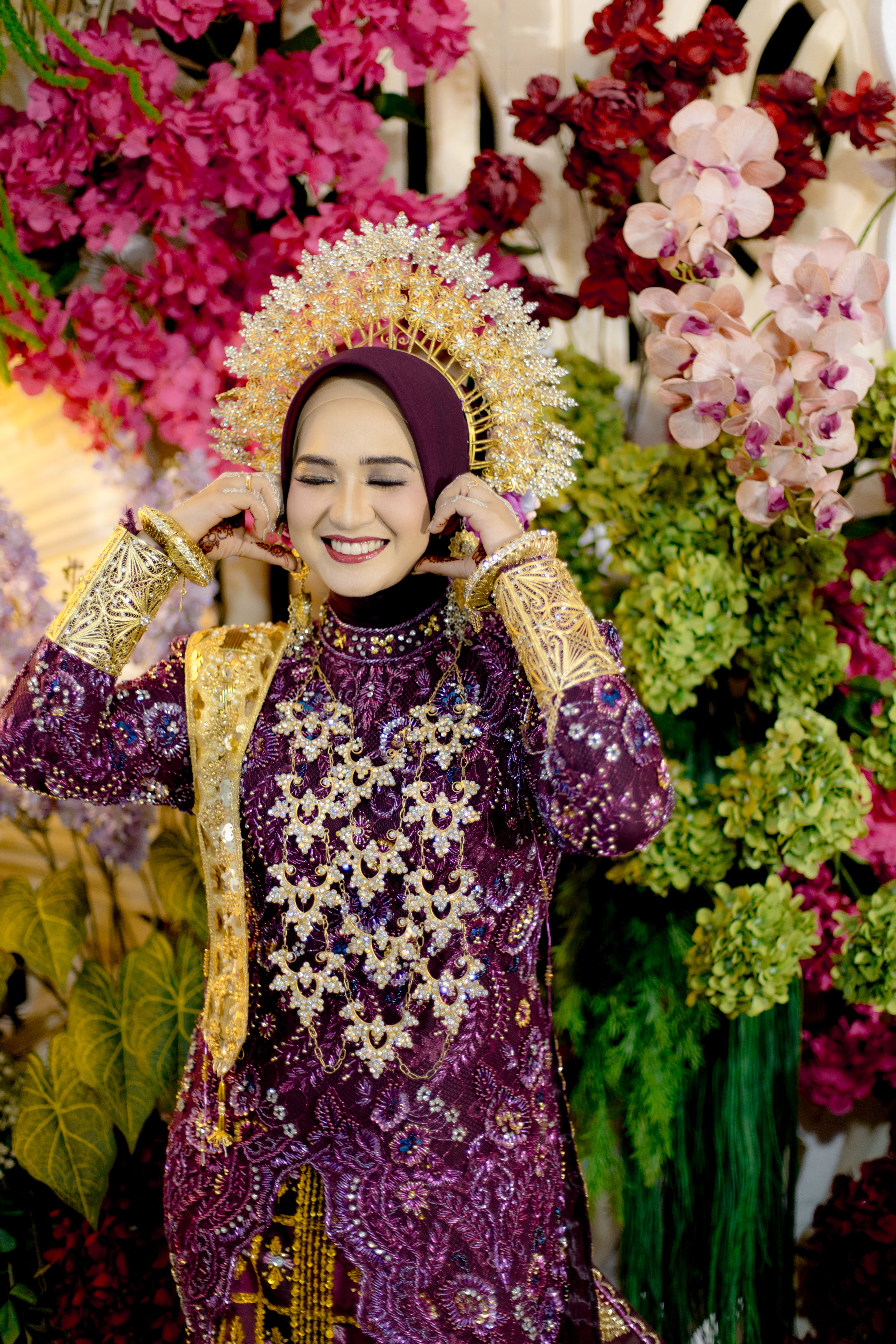 Smiling Indonesian bride in traditional dress with vibrant floral background.