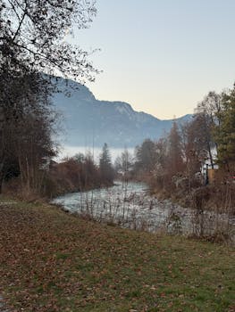 Peaceful winter scene by a river in Garmisch-Partenkirchen, Germany, with misty mountains.