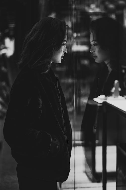거울 옆에 서있는 검은 재킷을 입은 여자