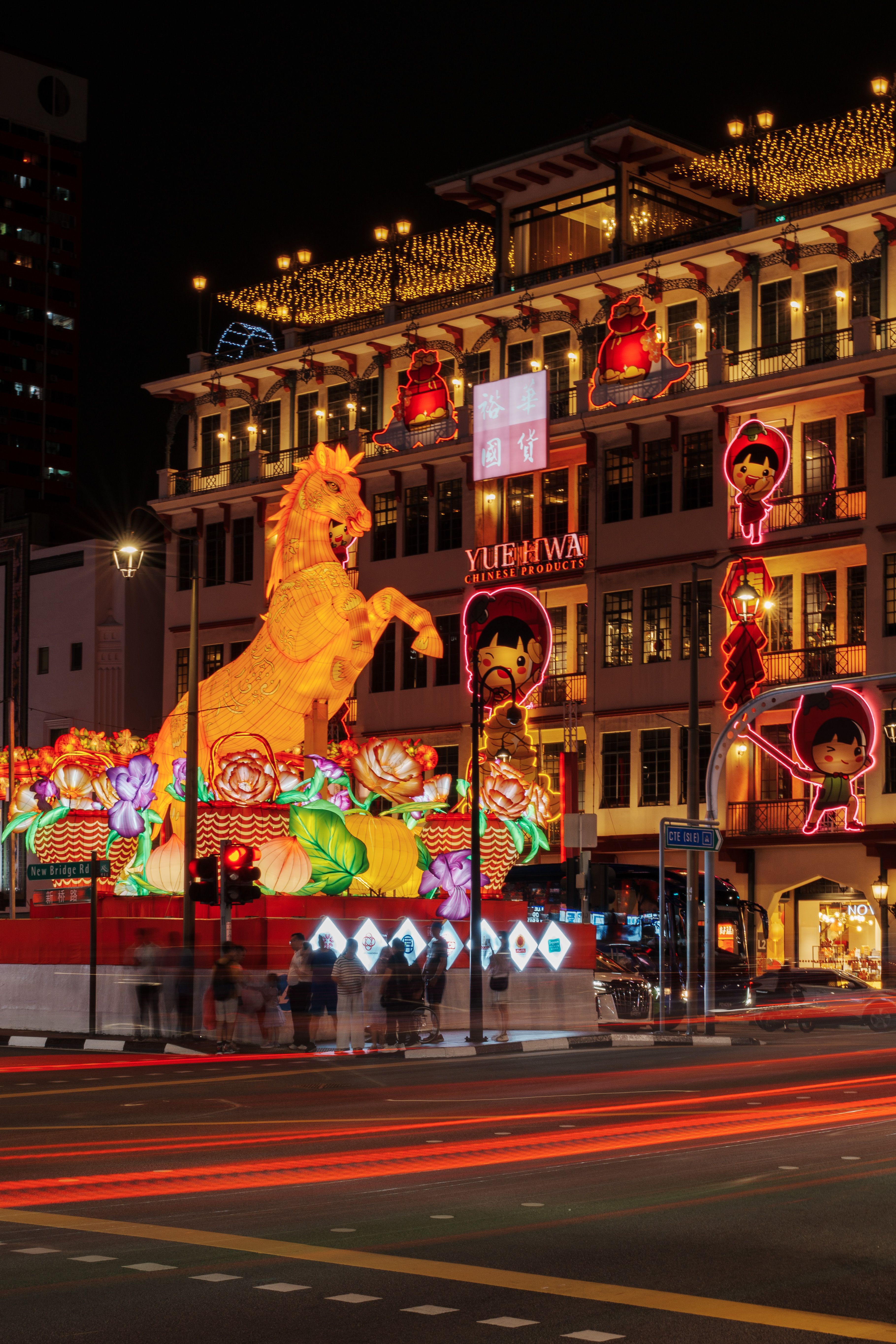 Illuminated Chinese New Year decorations with vibrant horse sculpture at night in a bustling urban setting.