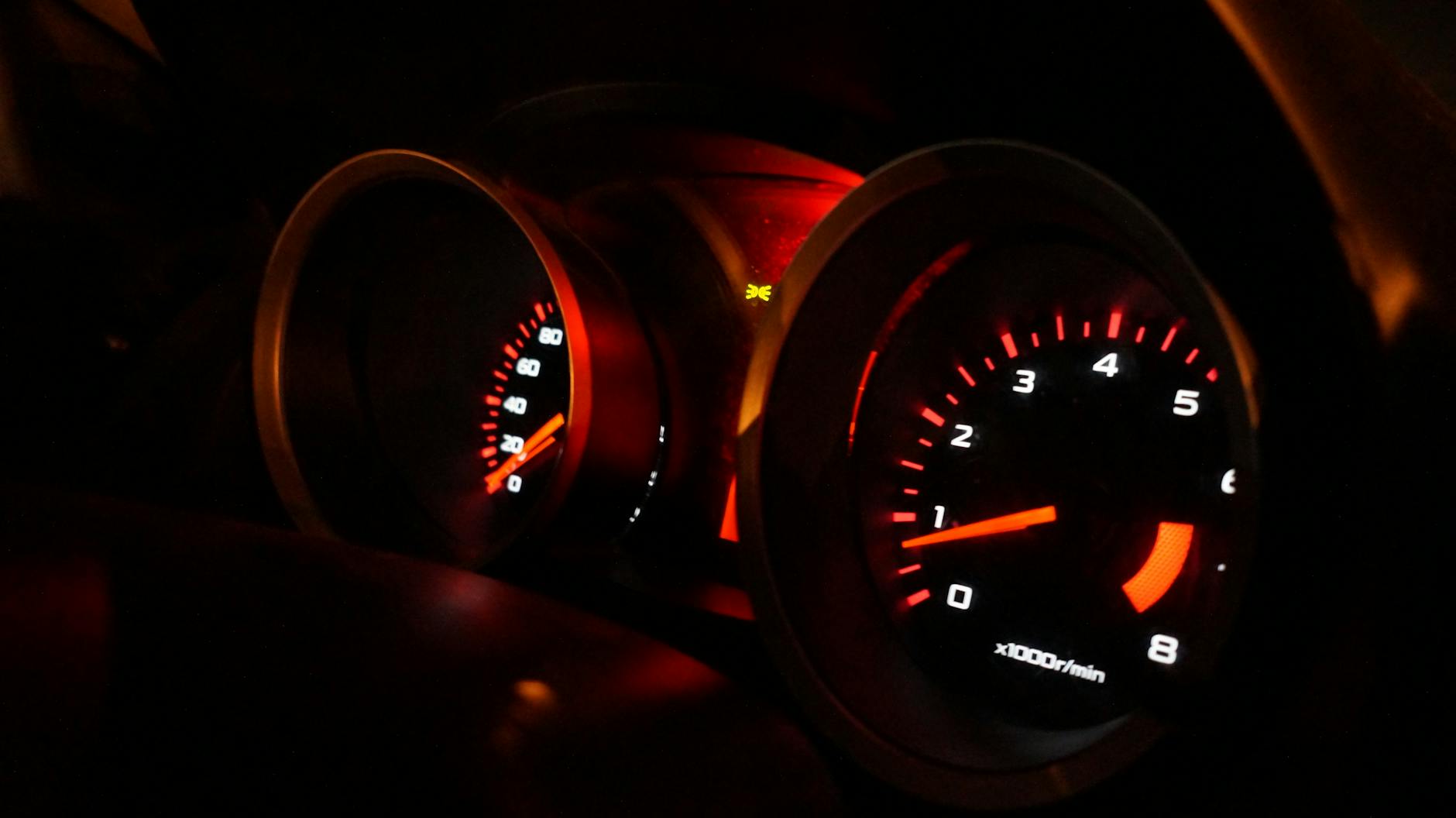 A detailed view of illuminated car gauges on the dashboard at night.