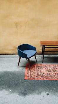 Minimalist interior with vintage blue chair, Persian rug, and simple wooden table.