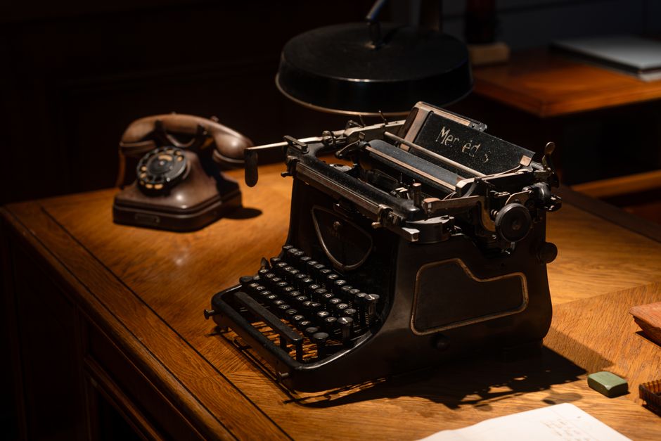 A classic scene featuring a vintage typewriter and rotary phone on a wooden desk, evoking nostalgia and history.
