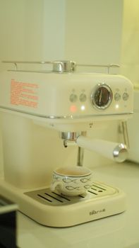 A vintage style espresso machine brewing coffee with a decorative cup underneath.