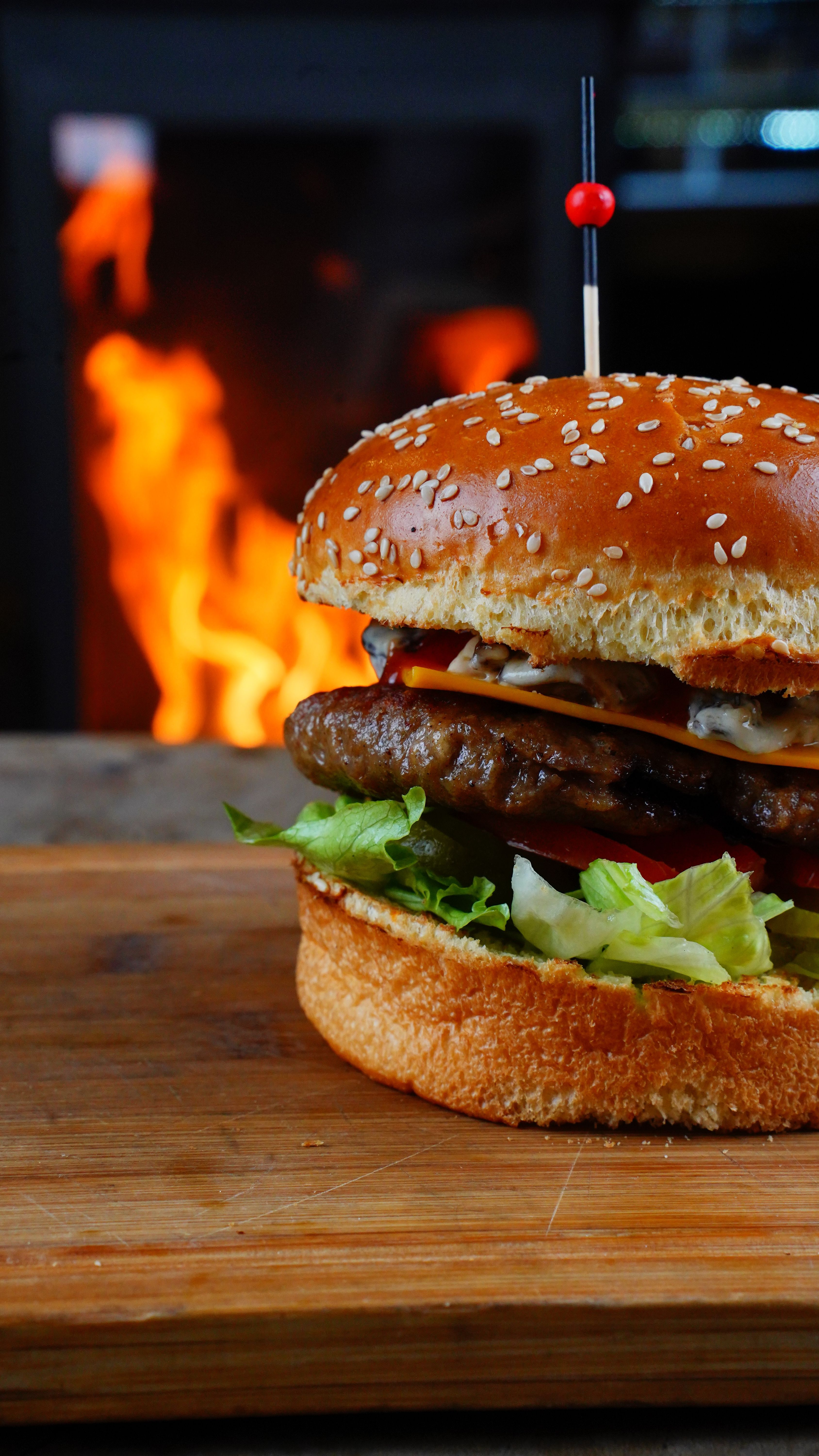 Delicious cheeseburger with fresh lettuce, tomatoes, and beef patty in front of a flaming backdrop.