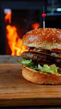 Delicious cheeseburger with fresh lettuce, tomatoes, and beef patty in front of a flaming backdrop.