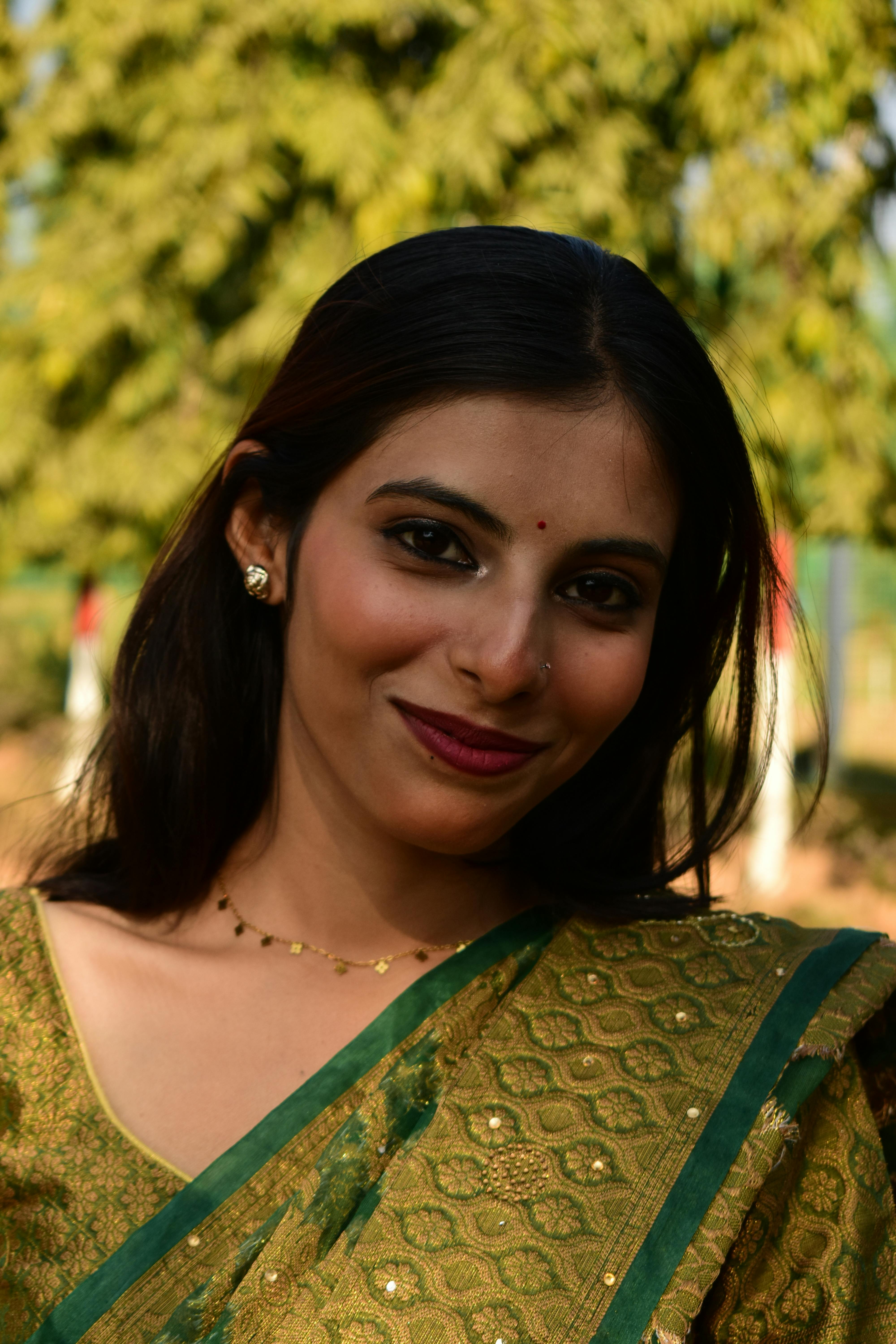 Portrait of a woman in a green sari with trees in the background.