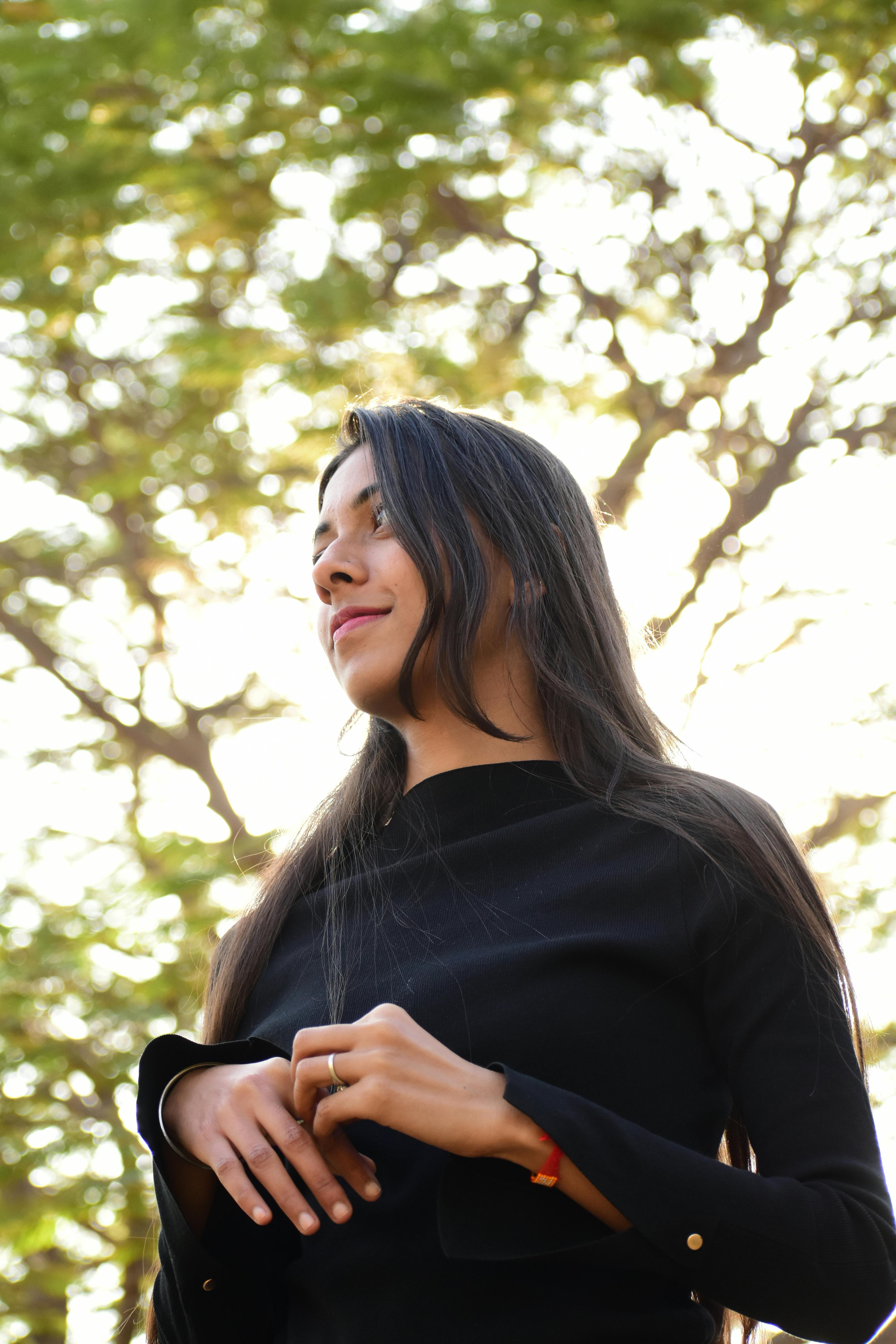 Portrait of a young woman in black, outdoors with backlit trees.