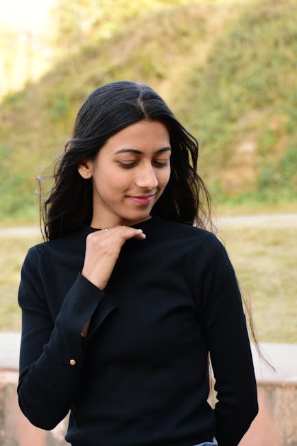 A young woman in black shirt smiling outdoors in a serene natural setting.