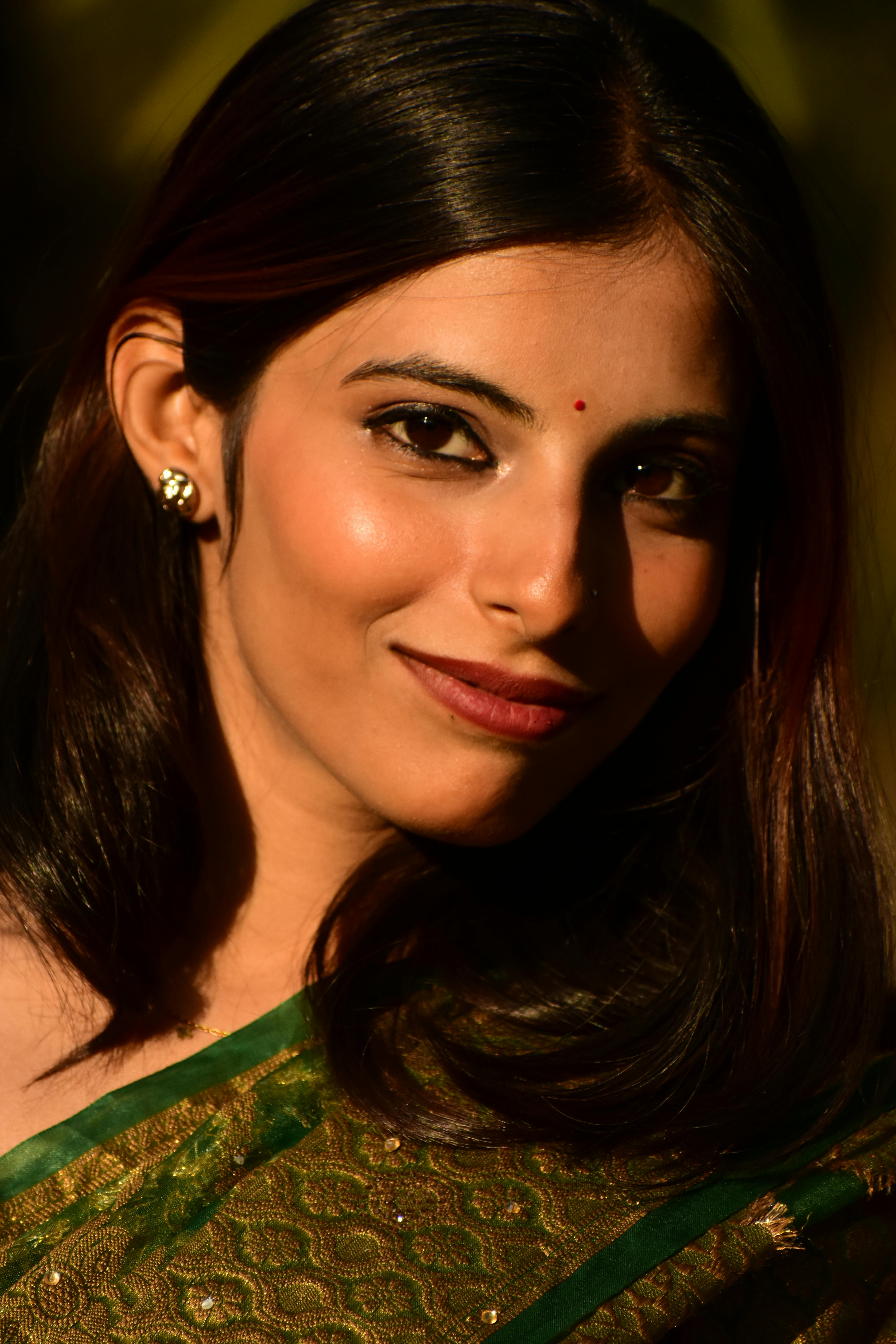 Close-up portrait of a woman wearing a green saree, captured in warm sunlight.