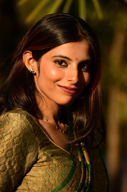 A woman wearing traditional attire smiles warmly outdoors in golden sunlight.