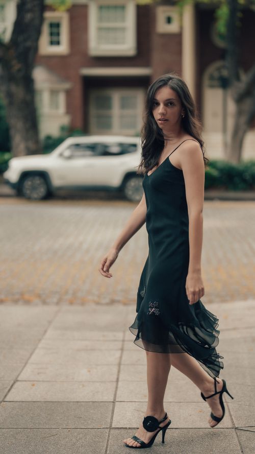 Free Stylish woman in black dress walking confidently on an urban sidewalk. Stock Photo