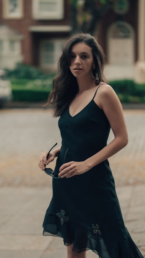 Free Elegant woman in a black dress holding sunglasses on a city street during the day. Stock Photo