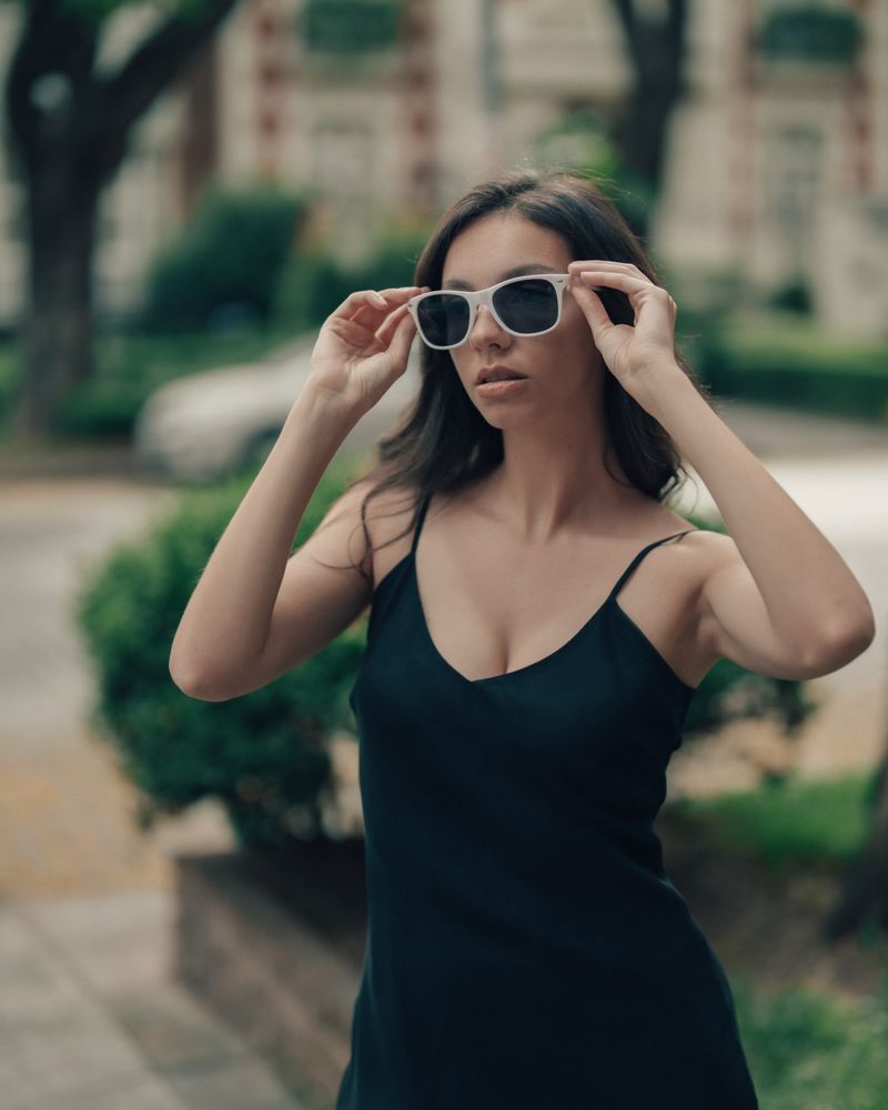 Woman in a black dress adjusting sunglasses outdoors, photo by Guillermo Berlin on Pexels