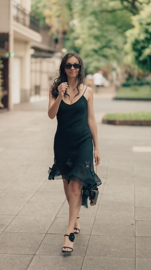 Free Confident woman in black dress and sunglasses strolling down a city street. Stock Photo