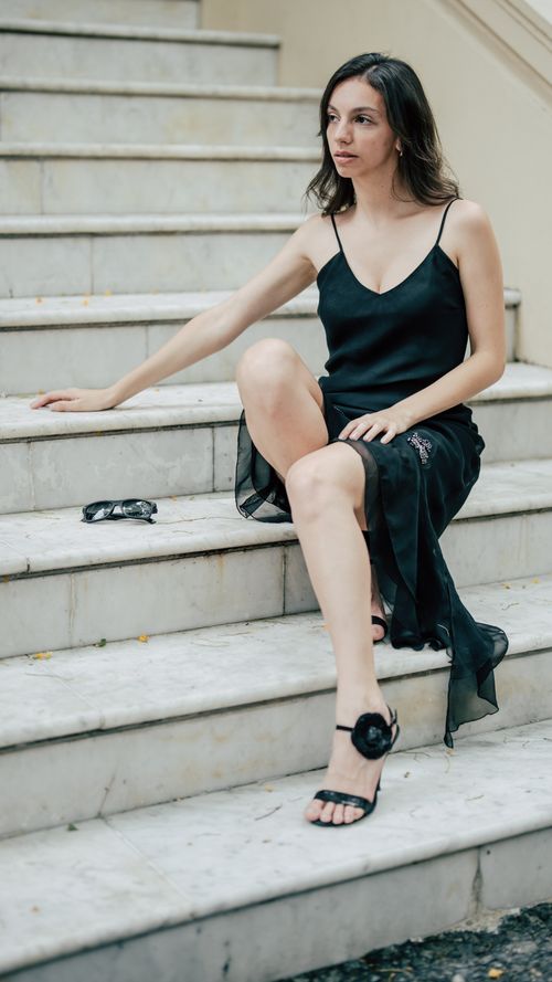 Free A woman in a black dress sits gracefully on marble stairs, exuding elegance. Stock Photo