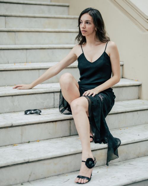 Free Stylish woman wearing a black dress sitting on marble steps, exuding elegance and sophistication. Stock Photo