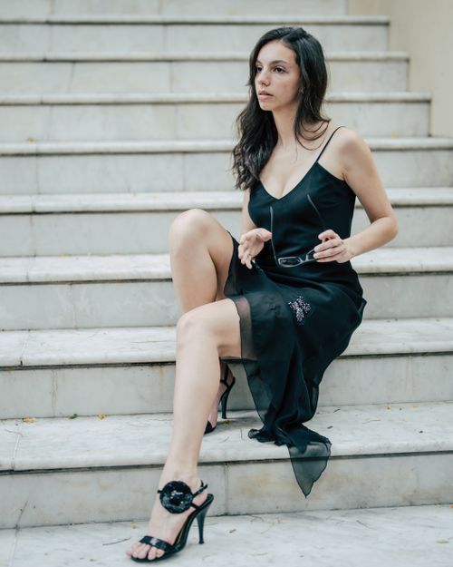 Free Stylish woman in black dress seated on stairs, exuding elegance and sophistication. Stock Photo