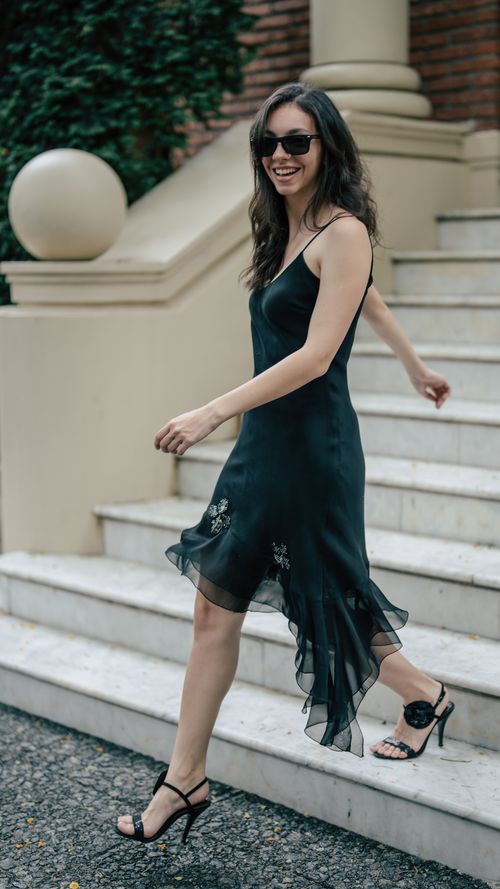 Free Smiling woman in stylish black dress and sunglasses walking down marble steps. Stock Photo