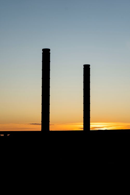 Free Silhouette of industrial chimneys against a vivid sunset sky, creating a dramatic industrial scene. Stock Photo